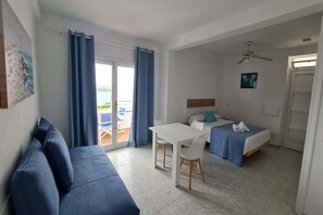A room with a bed, a sofa, a table, and a ceiling fan. - Vistamar Apartments (Es Migjorn Gran)