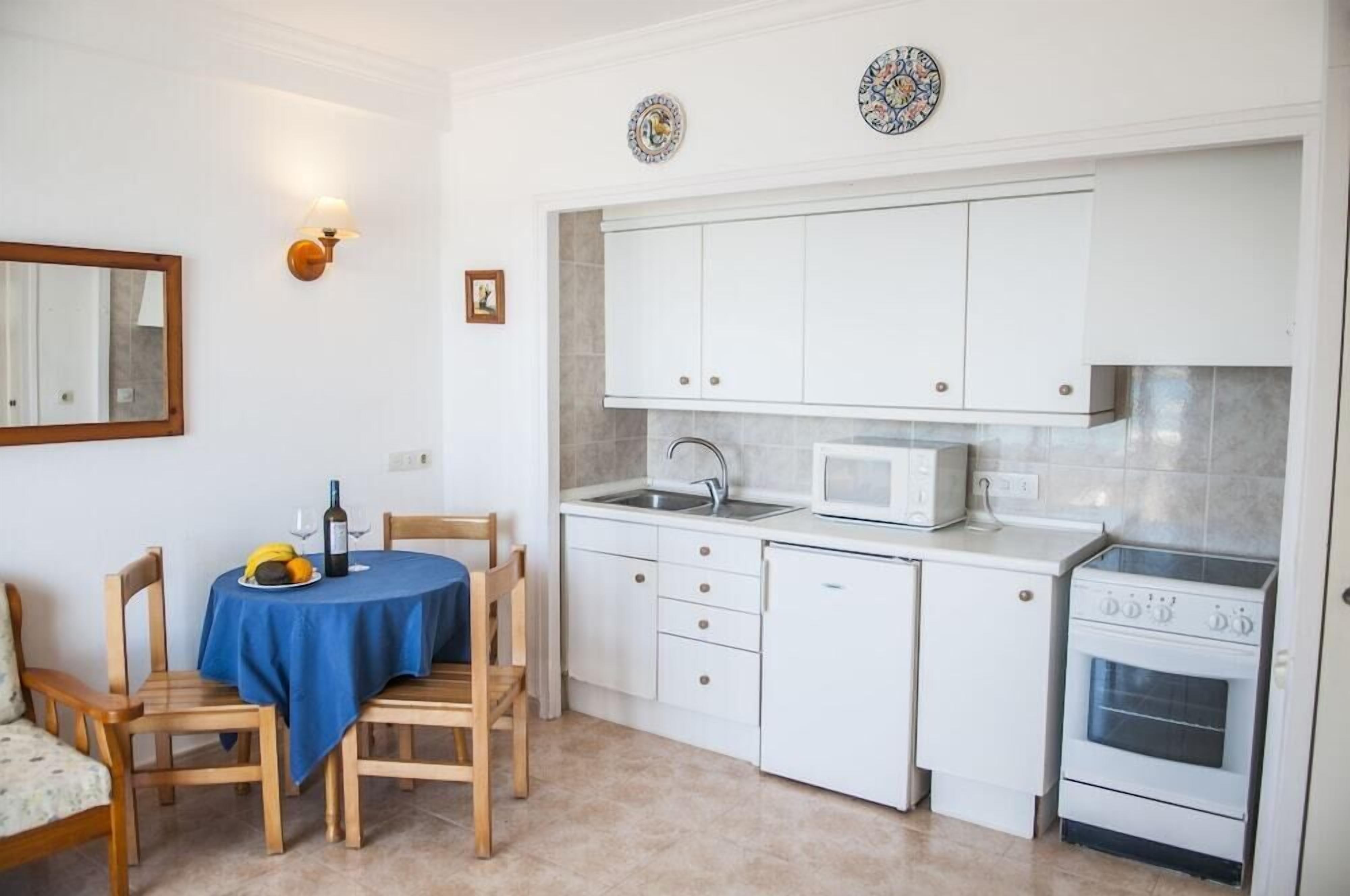 A compact kitchen with white cabinets, a microwave, a sink, and an oven. There is a dining table with a blue tablecloth and chairs.