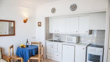 A compact kitchen with white cabinets, a microwave, a sink, and an oven. There is a dining table with a blue tablecloth and chairs.