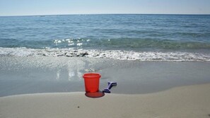 Una playa con un cubo rojo y una pala azul sobre la arena.
