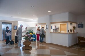 Un hall de hotel con mostrador de recepción, zona de espera con mesa redonda y mostrador de check-in.