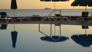 Piscina infinita con sillas de descanso y sombrillas, con vista al mar.
