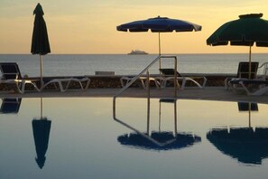 Une piscine à débordement avec des chaises longues et des parasols, offrant une vue sur la mer.