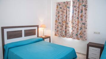 Un dormitorio con cama, mesita de noche, lámpara y ventana con cortinas estampadas.