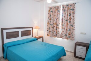 Un dormitorio con cama, mesita de noche, lámpara y ventana con cortinas estampadas.