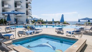 A pool area with lounge chairs and umbrellas, a dolphin mosaic, and a view of the ocean. - Vistamar Apartments (Es Migjorn Gran)