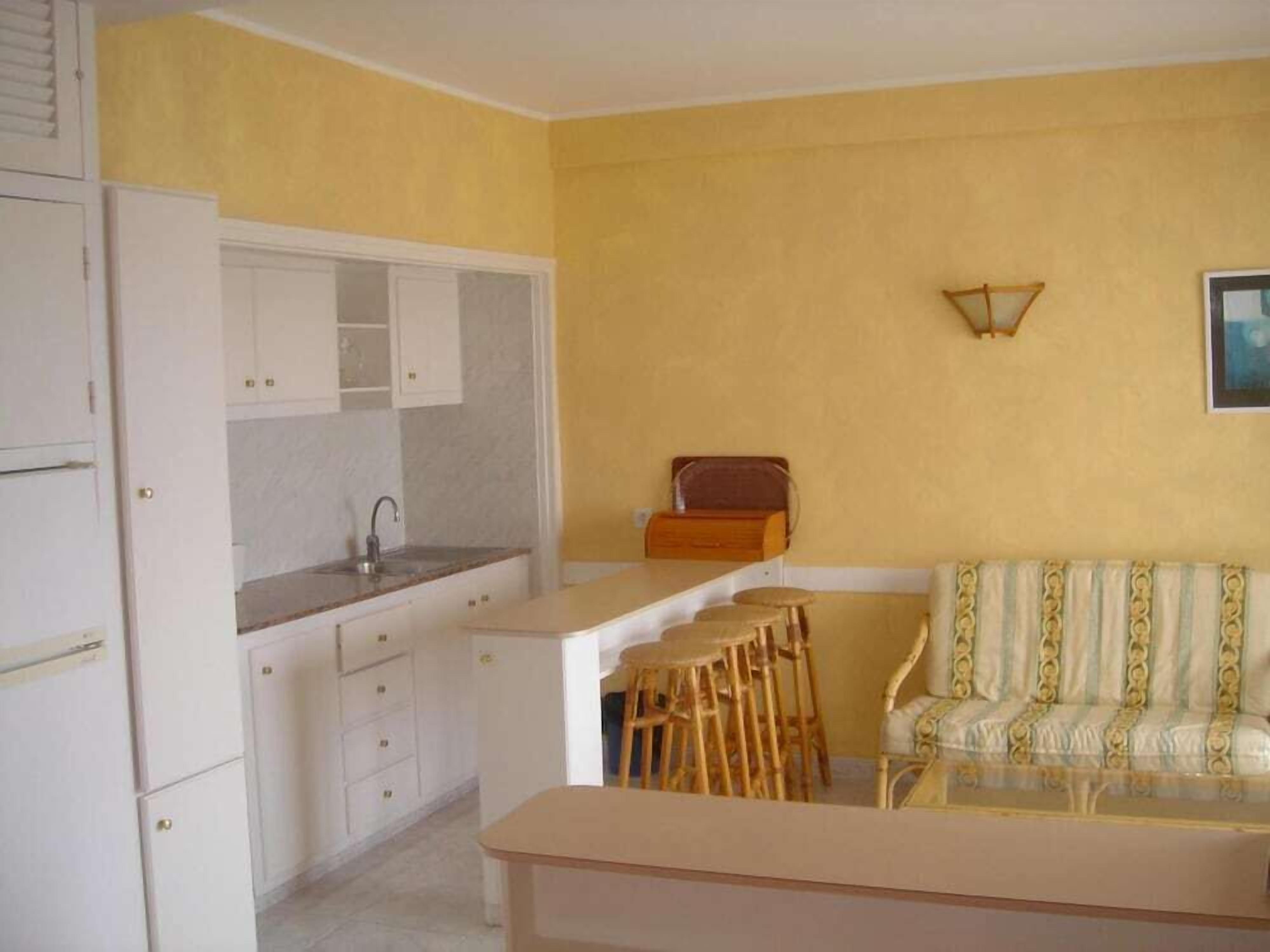 Un espacio habitable compacto con kitchenette, un área de comedor con taburetes y un sofá.