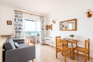 Una habitación con sofá, mesa de comedor, sillas, un mueble bajo y vista al mar a través de una puerta.