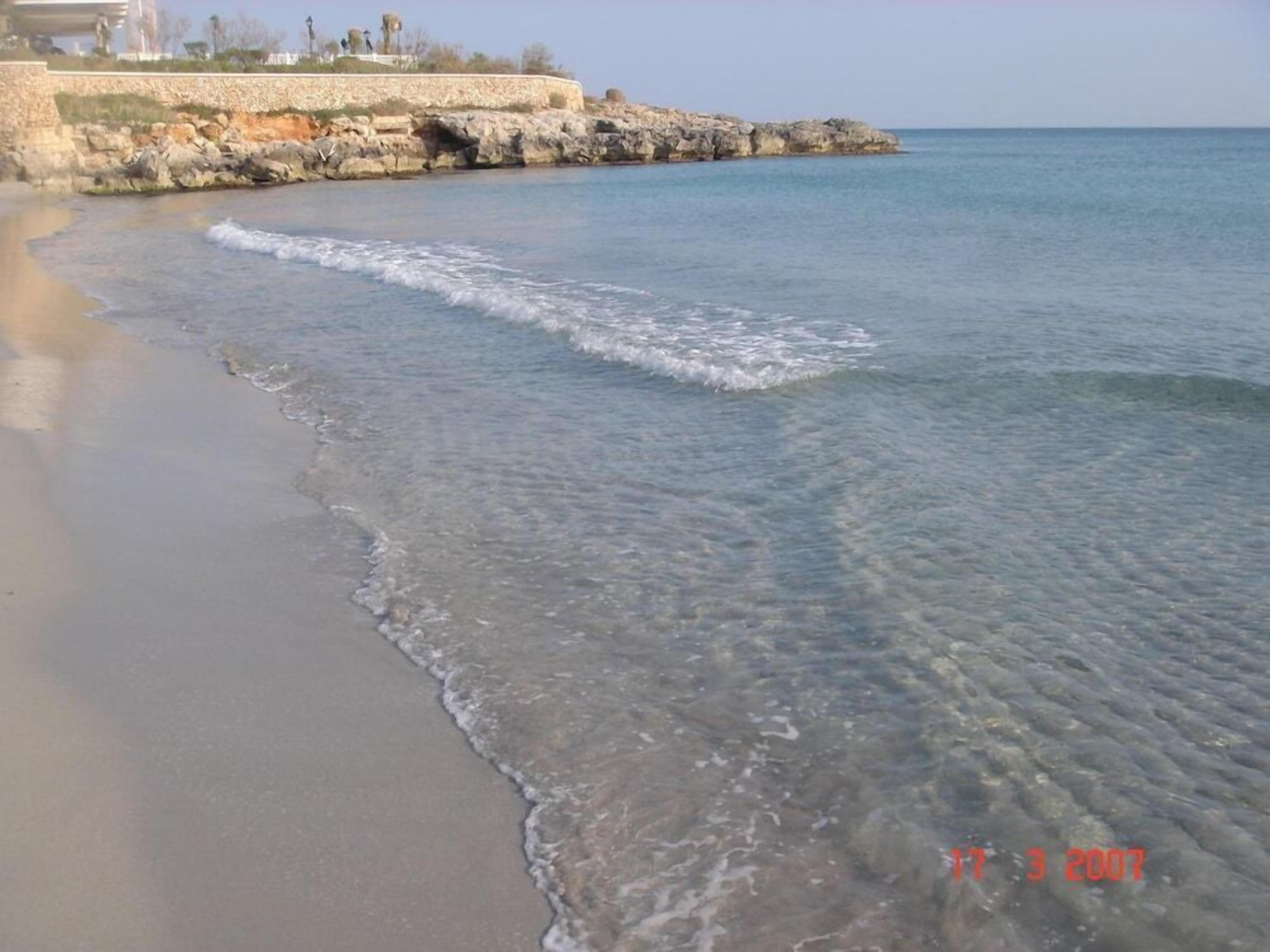 Una playa con agua cristalina, costa rocosa y un muro de piedra.
