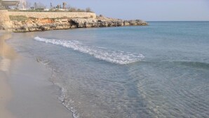 A beach with clear water, a rocky shoreline, and a stone wall. - Vistamar Apartments (Es Migjorn Gran)