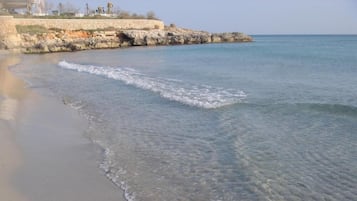 Una playa con agua cristalina, costa rocosa y un muro de piedra.