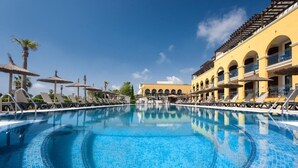 A swimming pool with lounge chairs and umbrellas, surrounded by yellow buildings with arches. - Barcelo Costa Ballena Golf & Spa (Rota)