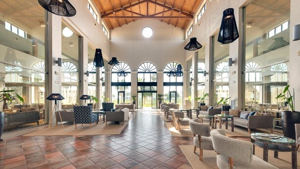 A spacious lobby with a high ceiling, large windows, and modern furniture. - Barcelo Costa Ballena Golf & Spa (Rota)