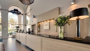 A modern reception desk with a light wood finish, a black lamp, and a vase with flowers. - Barcelo Costa Ballena Golf & Spa (Rota)