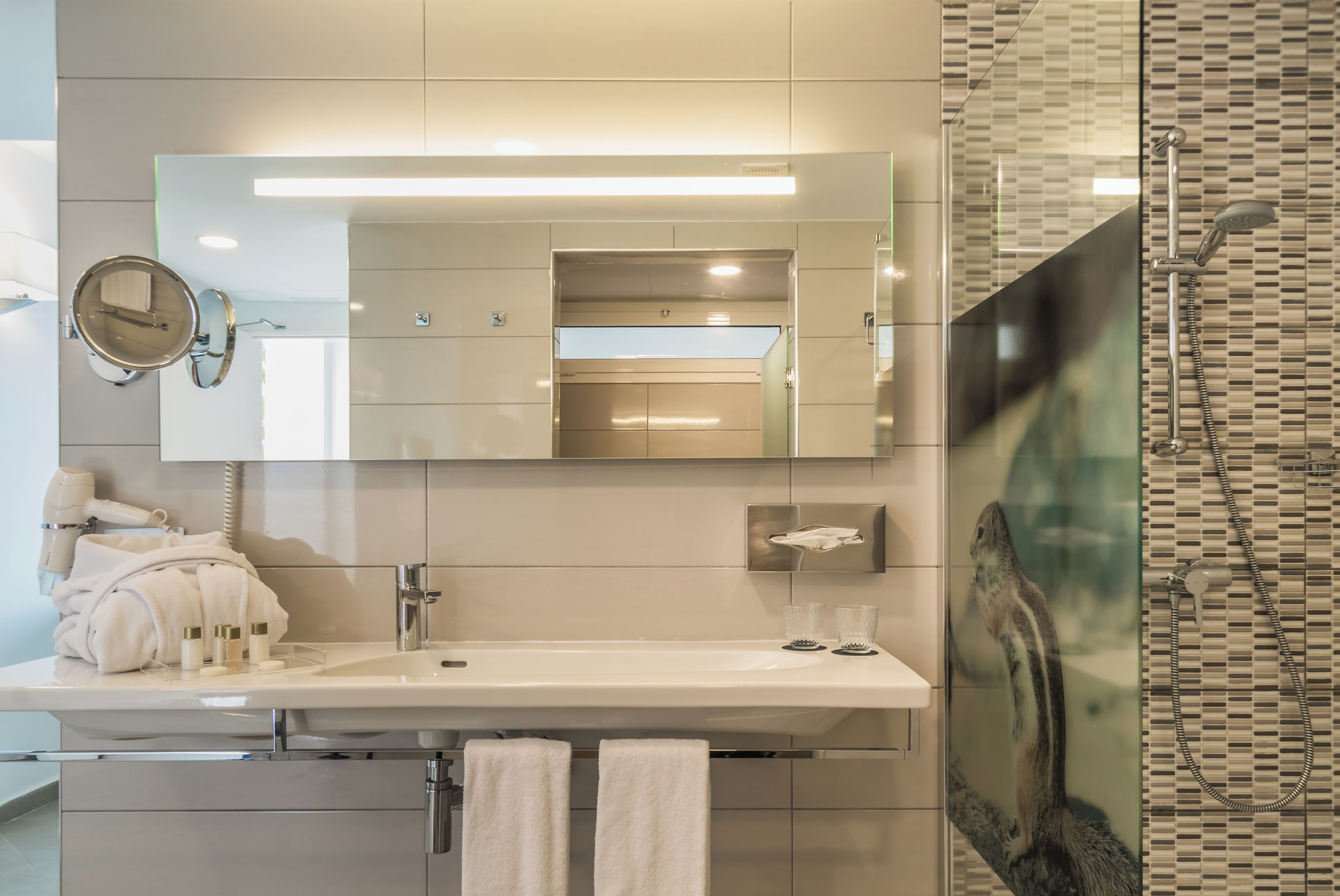Un baño moderno con un espejo grande, un lavamanos y una zona de ducha.