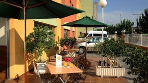 Una terrazza esterna con tavoli e sedie, ombrelloni verdi e piante in vaso.