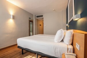Una habitación de hotel con una cama, mesita de noche y teléfono en la pared.