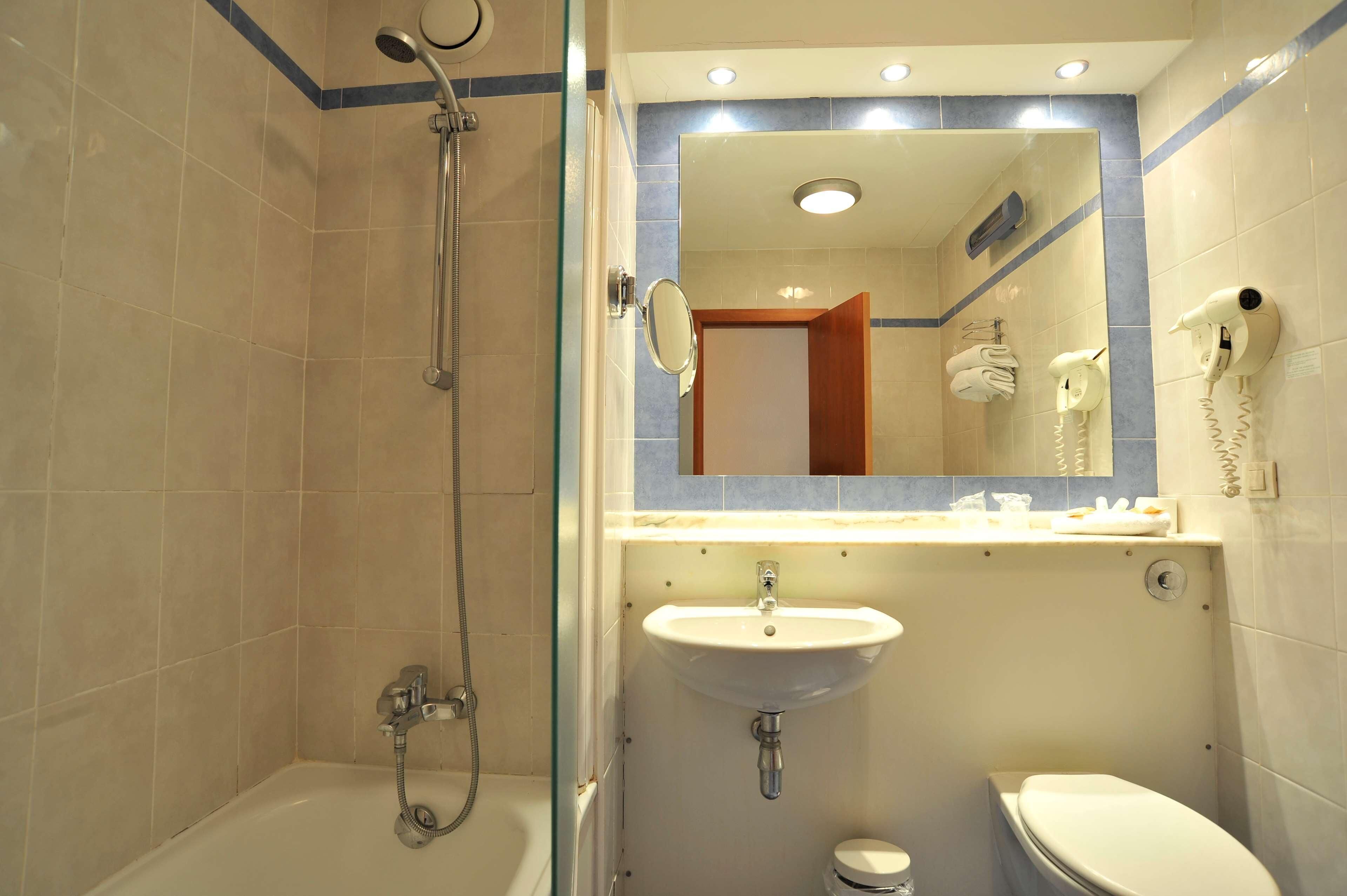 A bathroom with a shower, sink, toilet, and a mirror above the sink.