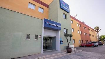 Un hotel Travelodge con fachada moderna, una zona de estacionamiento y un pequeño jardín con un banco.