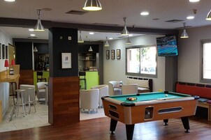 Mesa de billar en una sala con bar, asientos y televisor.
