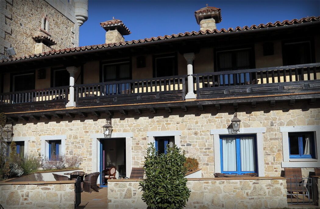 A stone building with a balcony, windows with blue shutters, and a small tree in the foreground.