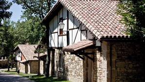 A row of traditional stone buildings with tiled roofs and timber framing, likely part of a historic village or tourist area.
