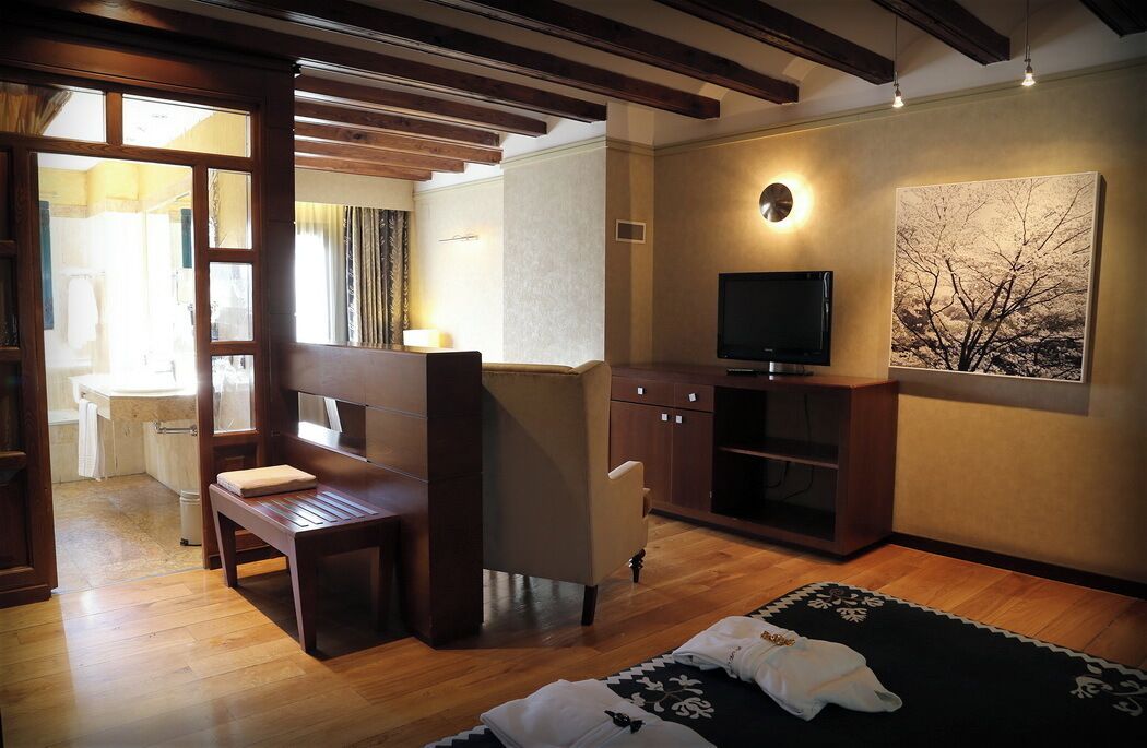 A room with a wooden bench, a television on a cabinet, and a painting on the wall.