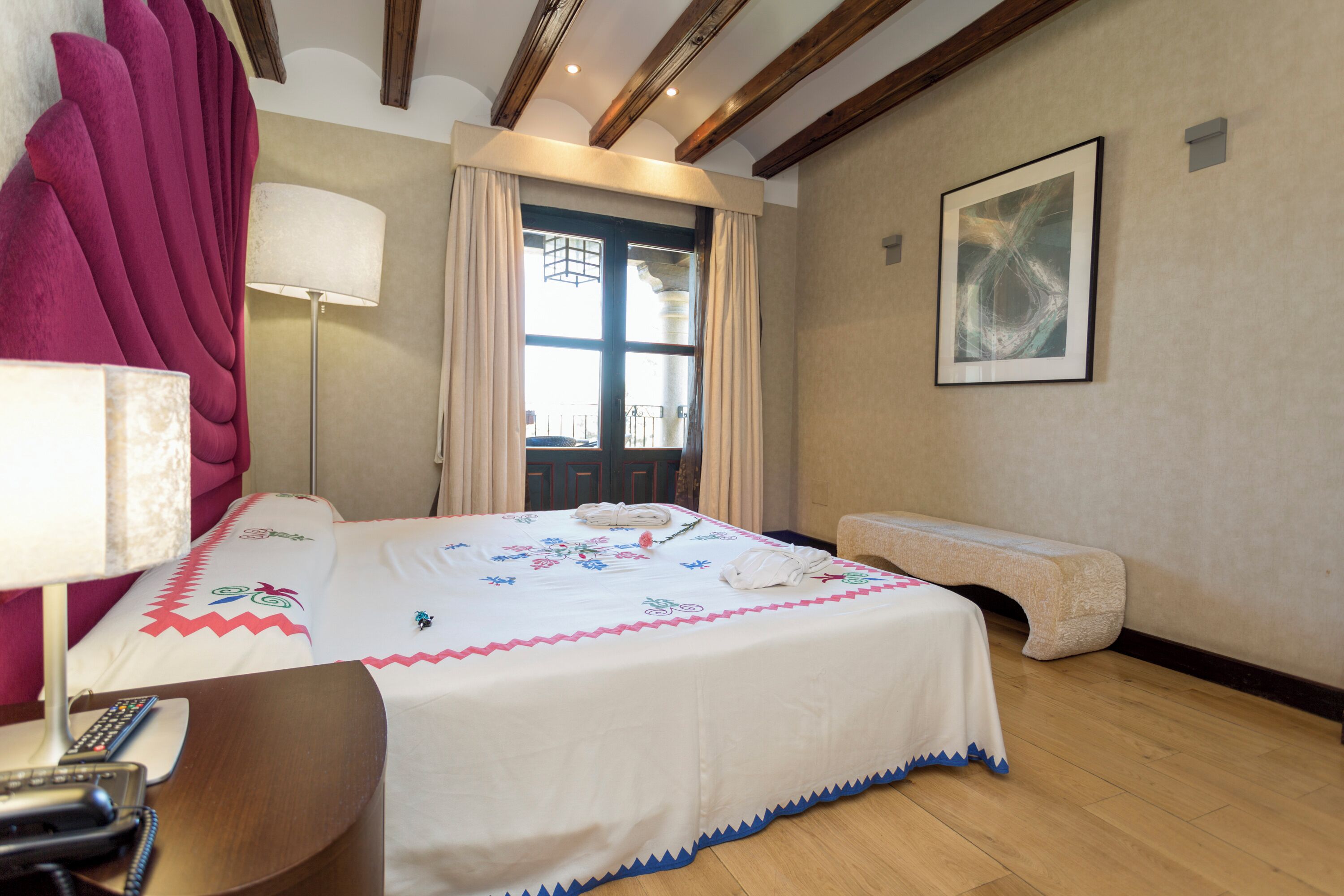 Une chambre d’hôtel avec un grand lit, une table de chevet avec une lampe, un banc et un tableau au mur.