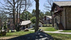 A traditional stone building with a wooden balcony, surrounded by trees and a well-maintained lawn.