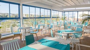 A restaurant with outdoor seating, large windows, and a view of the city. - Bimbolla Apartaments (Sant Lluis)