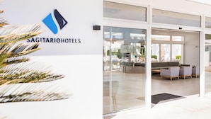 Entrada de hotel con diseño moderno, que incluye una recepción con asientos y una puerta de vidrio que da al interior.
