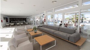 Un área de descanso moderna con un sofá gris, sillones blancos y mesas de madera.