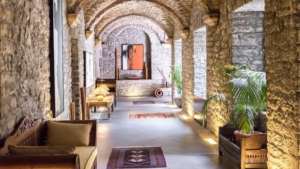 A stone-walled corridor with a sofa, a wooden bench, and a potted plant. - Hotel & Spa Monasterio de Boltana (Boltana)