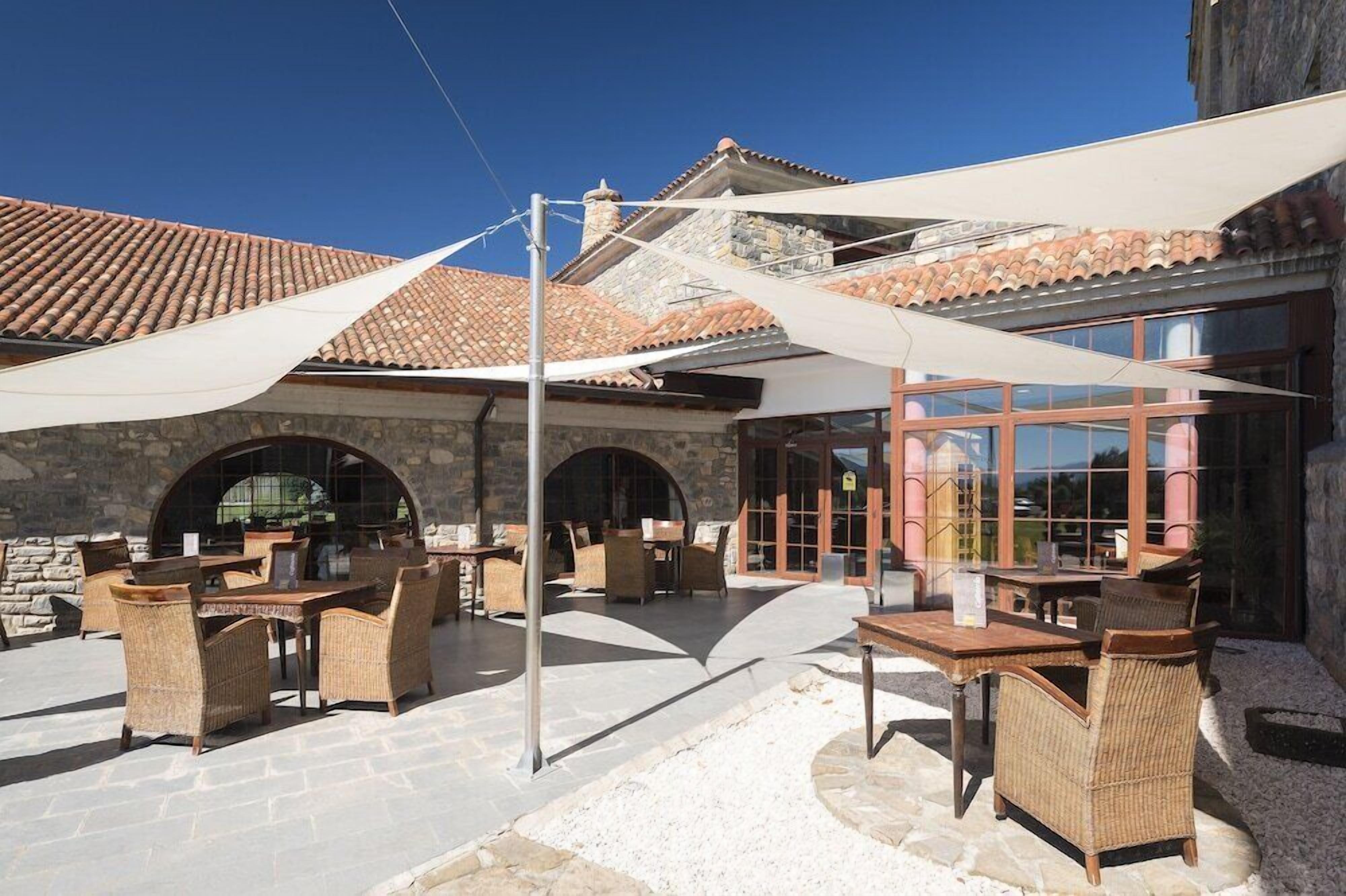 Un espacio al aire libre con patio, mobiliario de mimbre y un edificio de piedra al fondo.