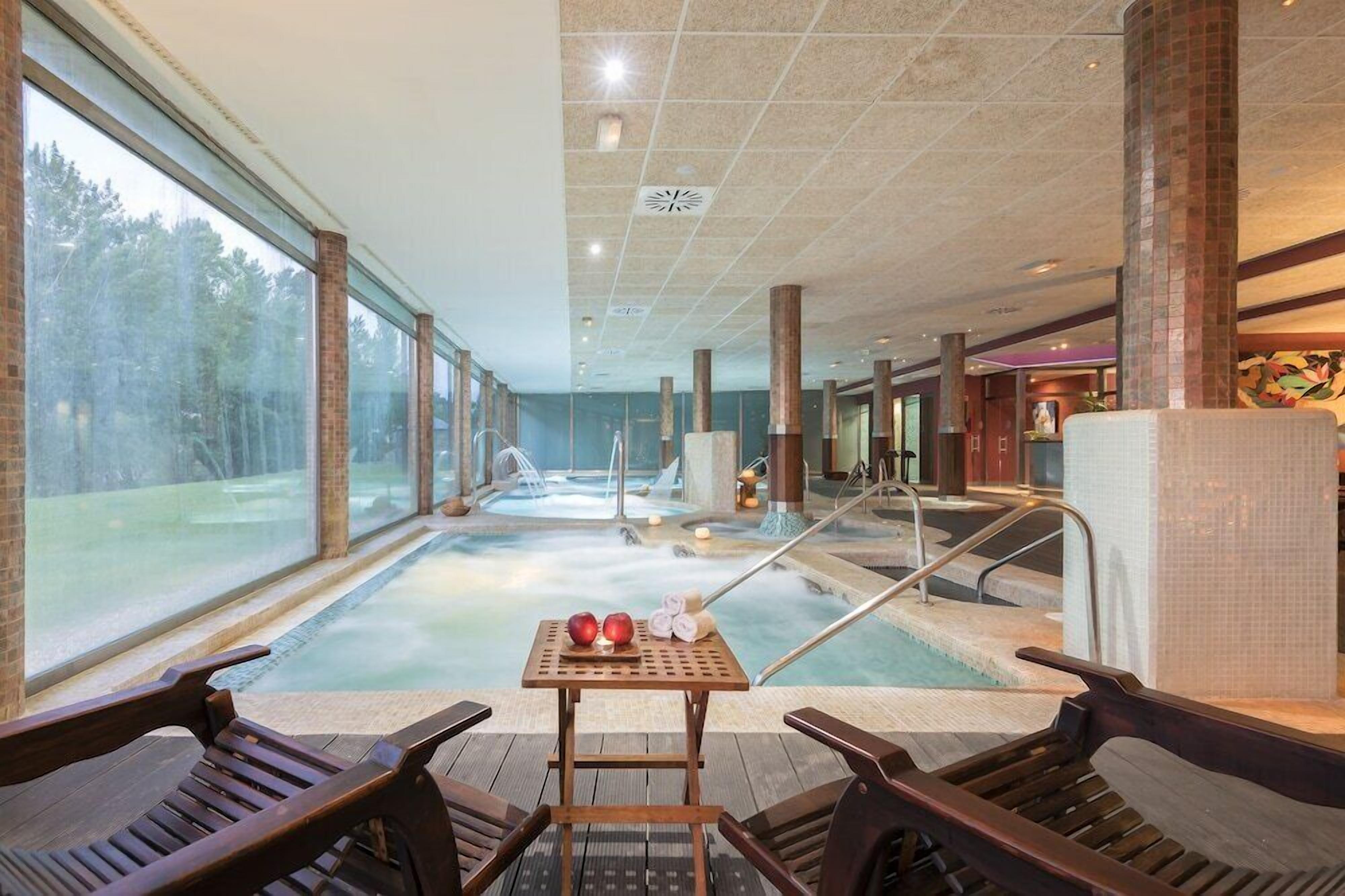 Un área de spa con una bañera de hidromasaje, sillas de madera y una mesa con toallas y manzanas.