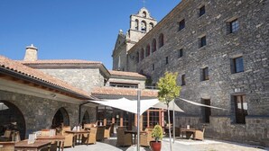 A courtyard with stone buildings, outdoor seating, and a bell tower. - Hotel & Spa Monasterio de Boltana (Boltana)