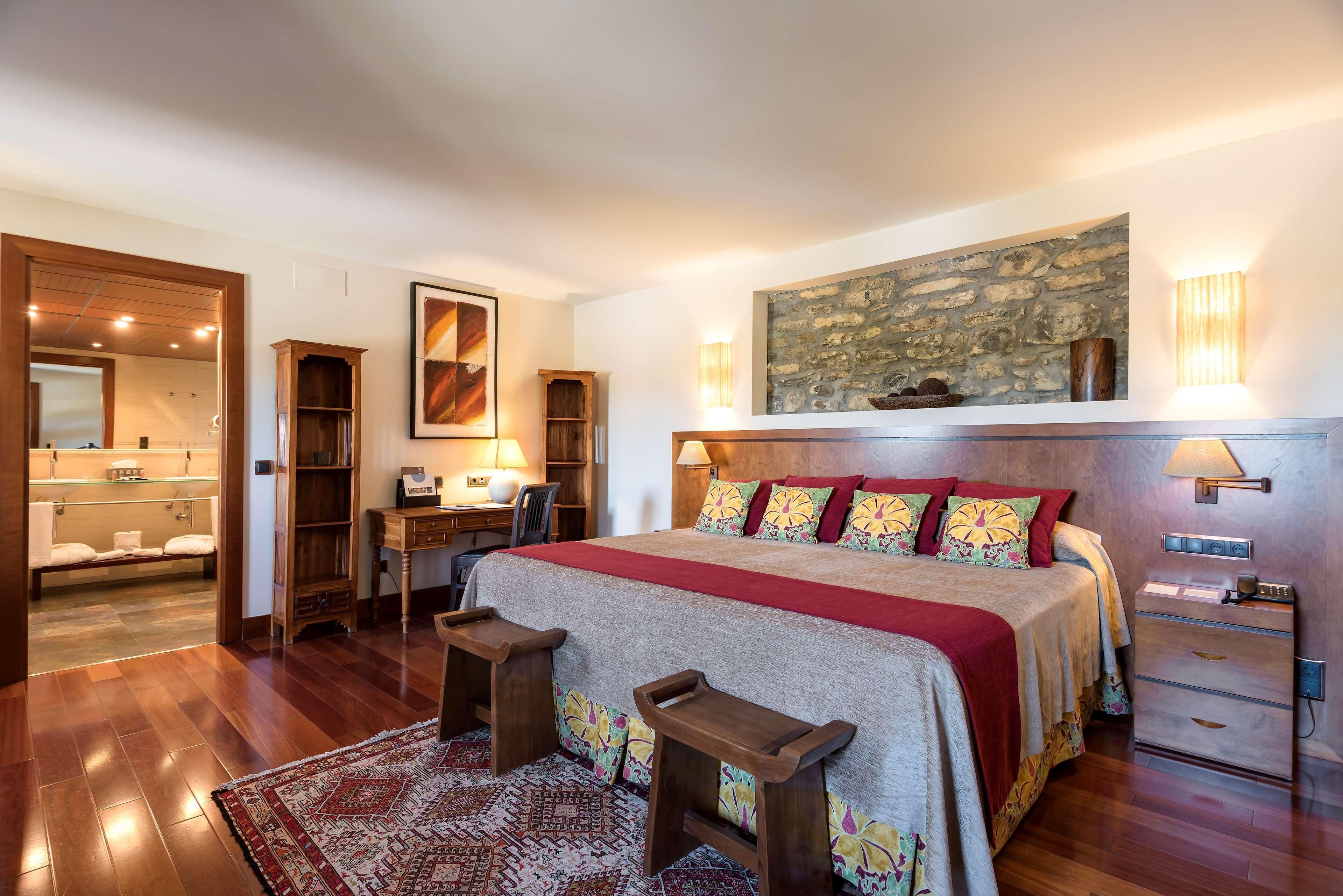 Un dormitorio con una cama grande, un escritorio y una silla. Se ve un baño a través de una puerta abierta.