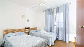 Ein Schlafzimmer mit zwei Betten, einem Deckenventilator und hellblauen Vorhängen.
