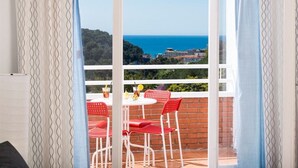 Ein Balkon mit Tisch und Stühlen, Blick auf das Meer und eine entfernte Landschaft.