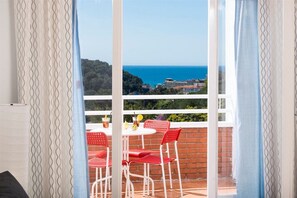 Ein Balkon mit Tisch und Stühlen, Blick auf das Meer und eine entfernte Landschaft.