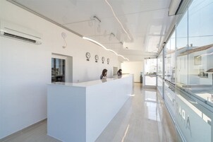 A modern reception area with a white reception desk, glass walls, and a clear view of the outside.