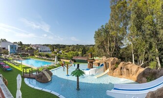 A swimming pool with a water slide, lounge chairs, and a view of surrounding buildings and trees.