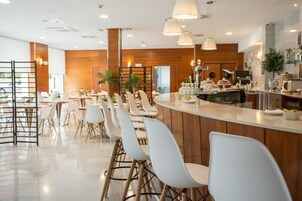 Un restaurante moderno con una barra alargada, sillas blancas e iluminación colgante.