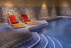 A spa area with a mosaic-tiled wall, two wooden loungers, and a curved pool edge. - Eurostars Royal Tanau (Naut Aran)