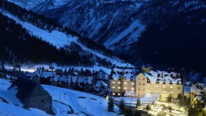 A snow-covered mountain village at dusk with a prominent hotel featuring multiple windows and a traditional architectural style. - Eurostars Royal Tanau (Naut Aran)