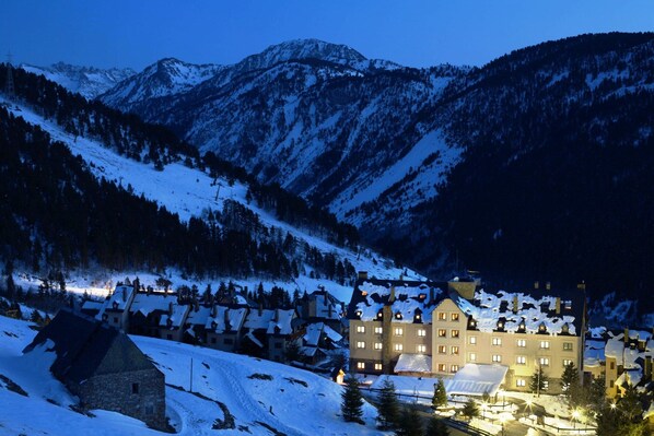 A snow-covered mountain village at dusk with a prominent hotel featuring multiple windows and a traditional architectural style. - Eurostars Royal Tanau (Naut Aran)