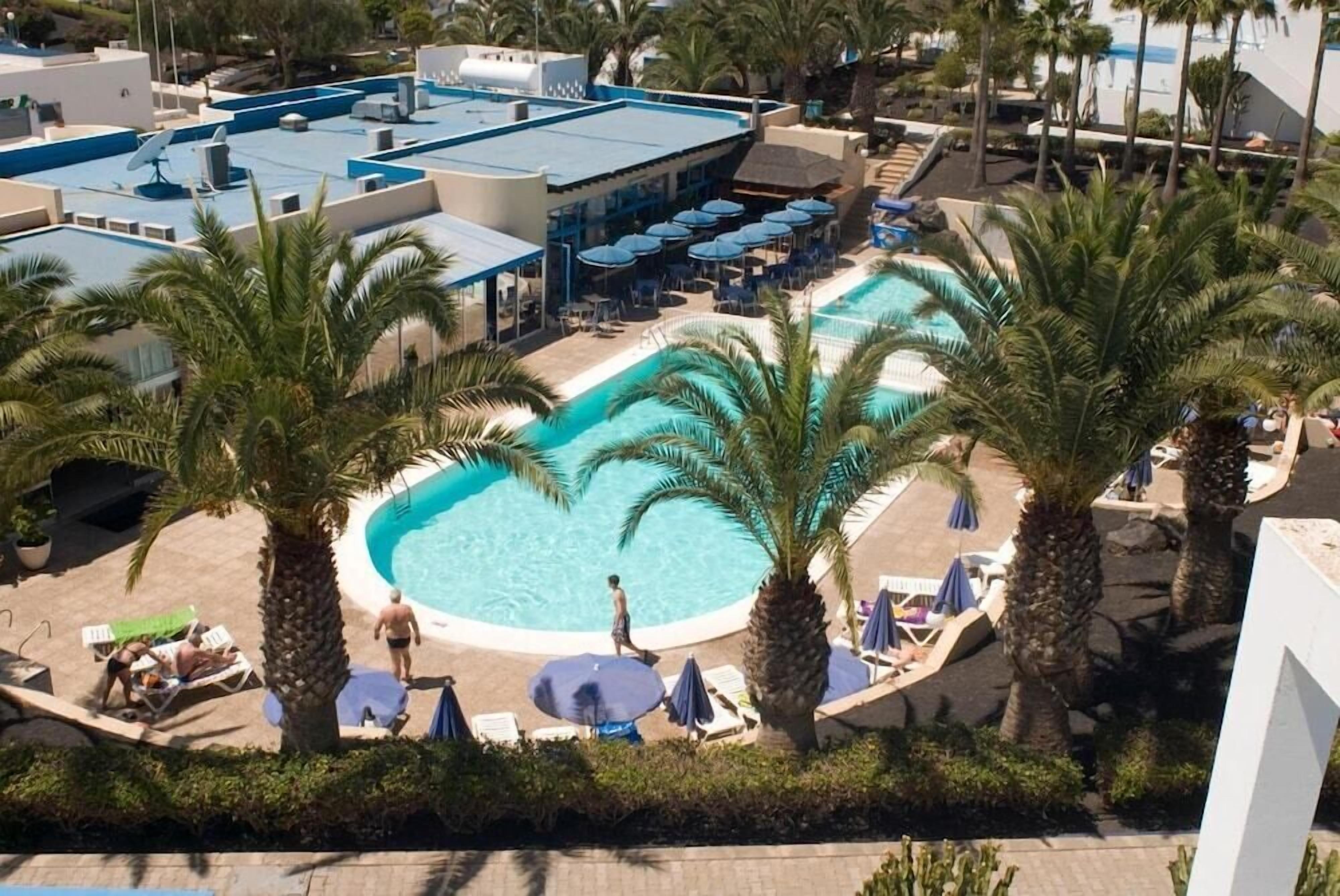 A rooftop pool area with multiple swimming pools, lounge chairs, and umbrellas.