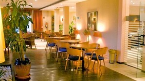 Un espace de restauration d’hôtel avec des tables et des chaises en bois, des plantes en pot et une cloison en verre.