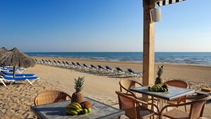 Un restaurante frente a la playa con terraza, una mesa llena de frutas y vistas al océano.