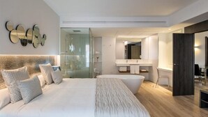 Un dormitorio moderno con una cama grande, cabina de ducha de vidrio, bañera y baño minimalista.